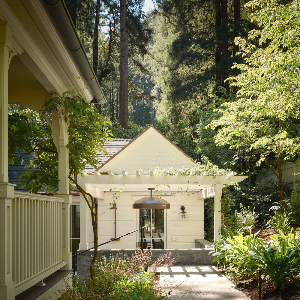 Blithedale Canyon guest house seen from the main house porch, with a wisteria-covered pergola, scalloped shingle gable and bluestone path leading through ferns beneath towering redwoods