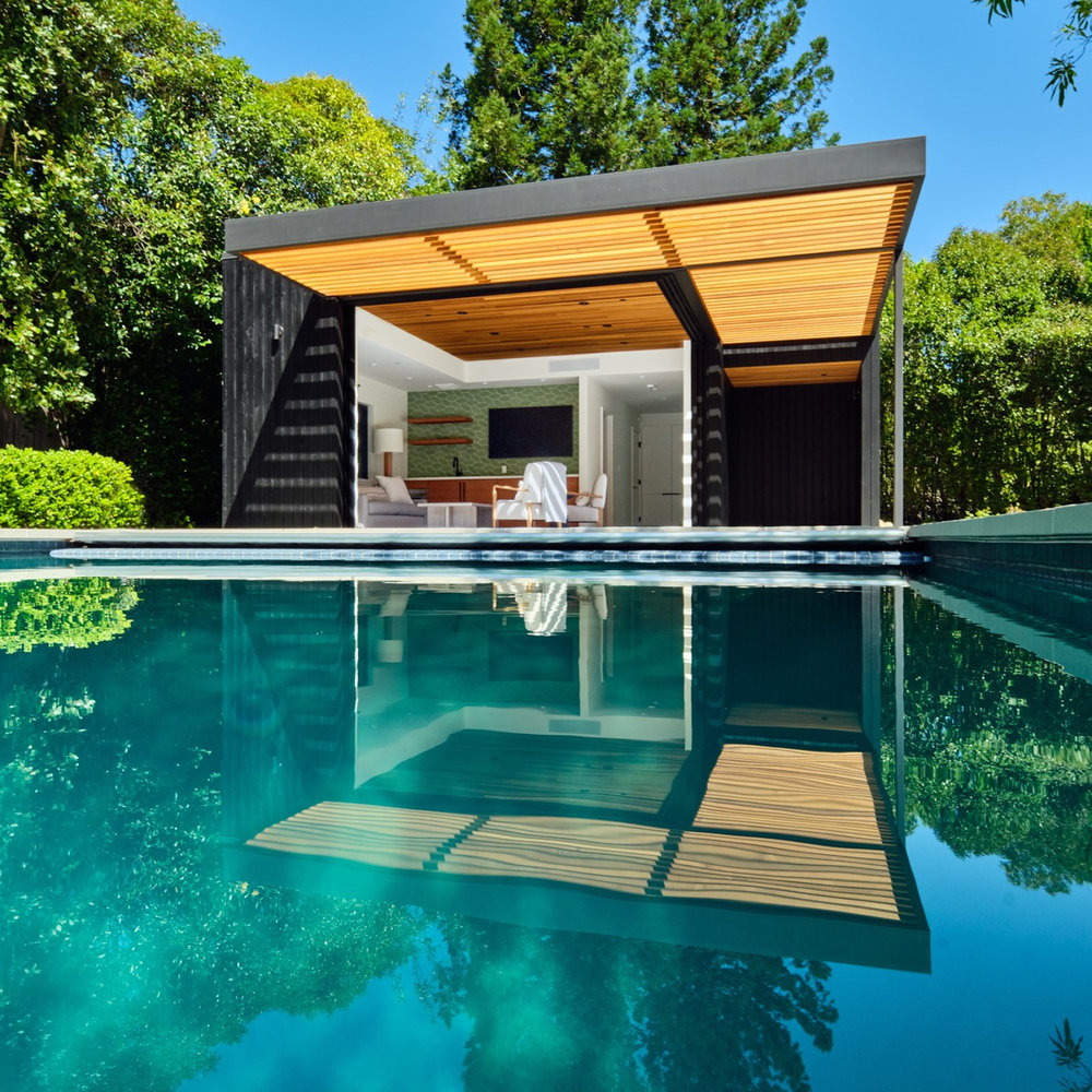 Modern ADU pool house in Sleepy Hollow Marin County featuring charred wood siding, floor-to-ceiling glass doors, and cantilevered wood soffit overlooking rectangular swimming pool