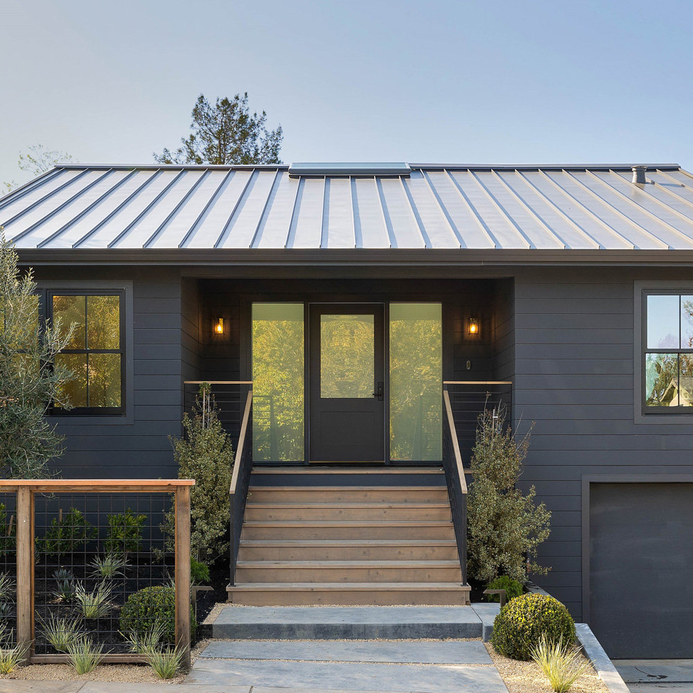 Sycamore Park 2 — Mill Valley modern farmhouse featuring dark gray siding, standing seam metal roof, skylights, indoor-outdoor kitchen, and landscaped backyard with pergola and guest house
