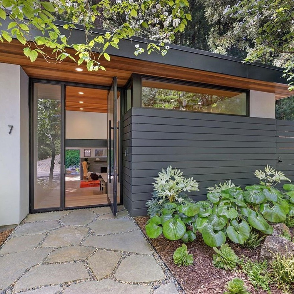 Warner Canyon mid-century modern home renovation in Marin County featuring exposed steel beams, open-plan kitchen with walnut cabinetry and marble island, skylights throughout, warm wood siding, and indoor-outdoor living spaces with fire pit and deck nestled among mature redwood trees
